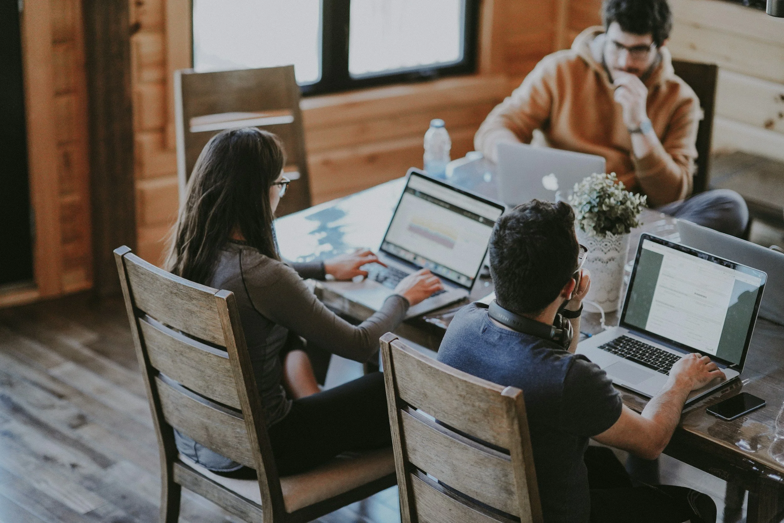 Three people working on laptops around a wooden table